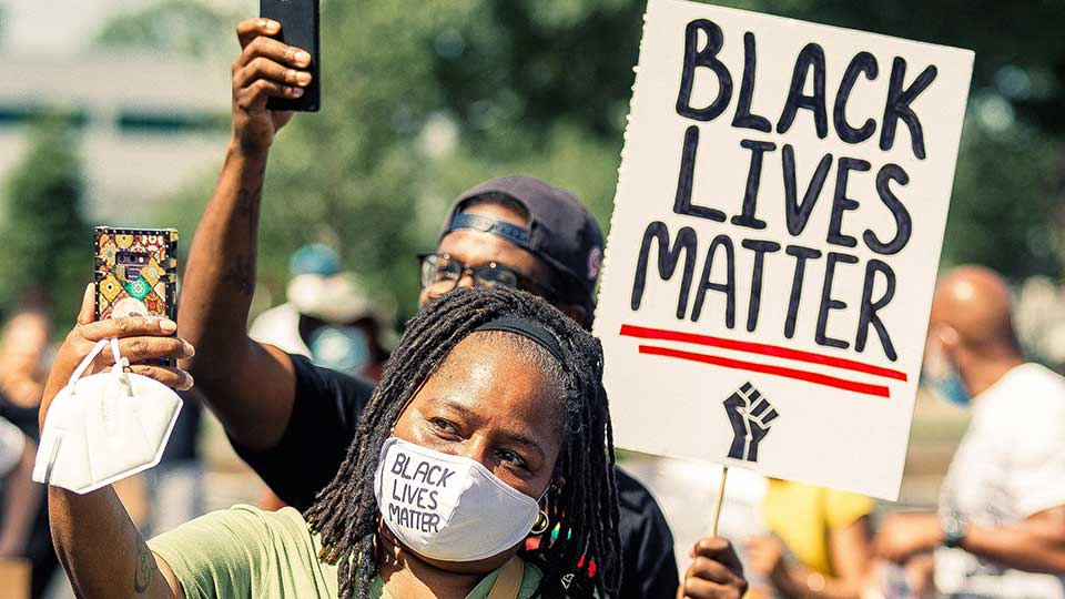 Woman at protest wearing facemask and holding Black Lives Matter placard.