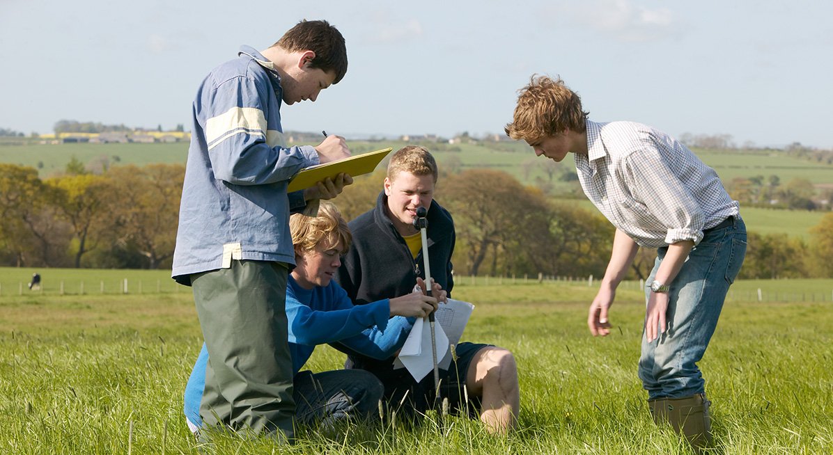 Students in a field looking at a data gathering instrument